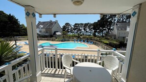 Un balcón con vista a una piscina, sillas blancas y una mesa.