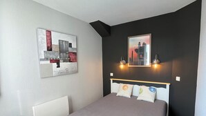 Un dormitorio con cama, mesitas de noche, un escritorio y obras de arte en las paredes.