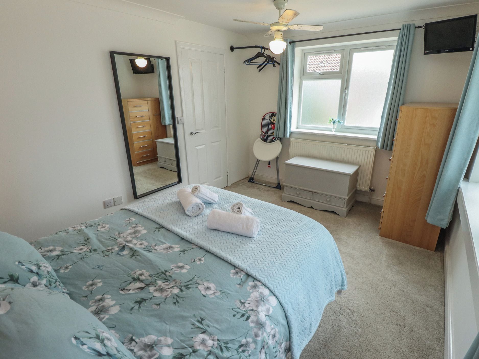 Un dormitorio con cama, cómoda, espejo, radiador y ventana con cortinas.