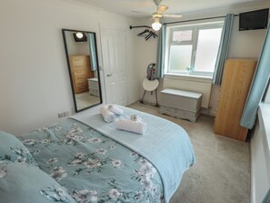 Une chambre à coucher avec un lit, une commode, un miroir, un radiateur et une fenêtre avec des rideaux.