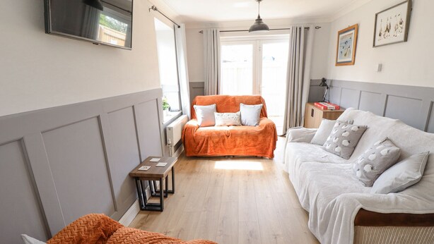 A cozy room with two sofas, a small table, and a TV on the wall.