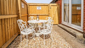 A patio with a round table and white chairs, surrounded by wooden fences and a brick wall.