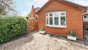 A red brick house with a bay window, a small garden with gravel paths, and a hedge.