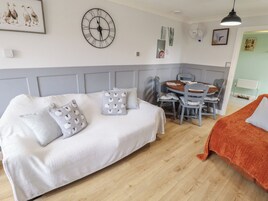 Una habitación acogedora con un sofá blanco, una mesa de comedor con sillas, un reloj en la pared y un radiador.