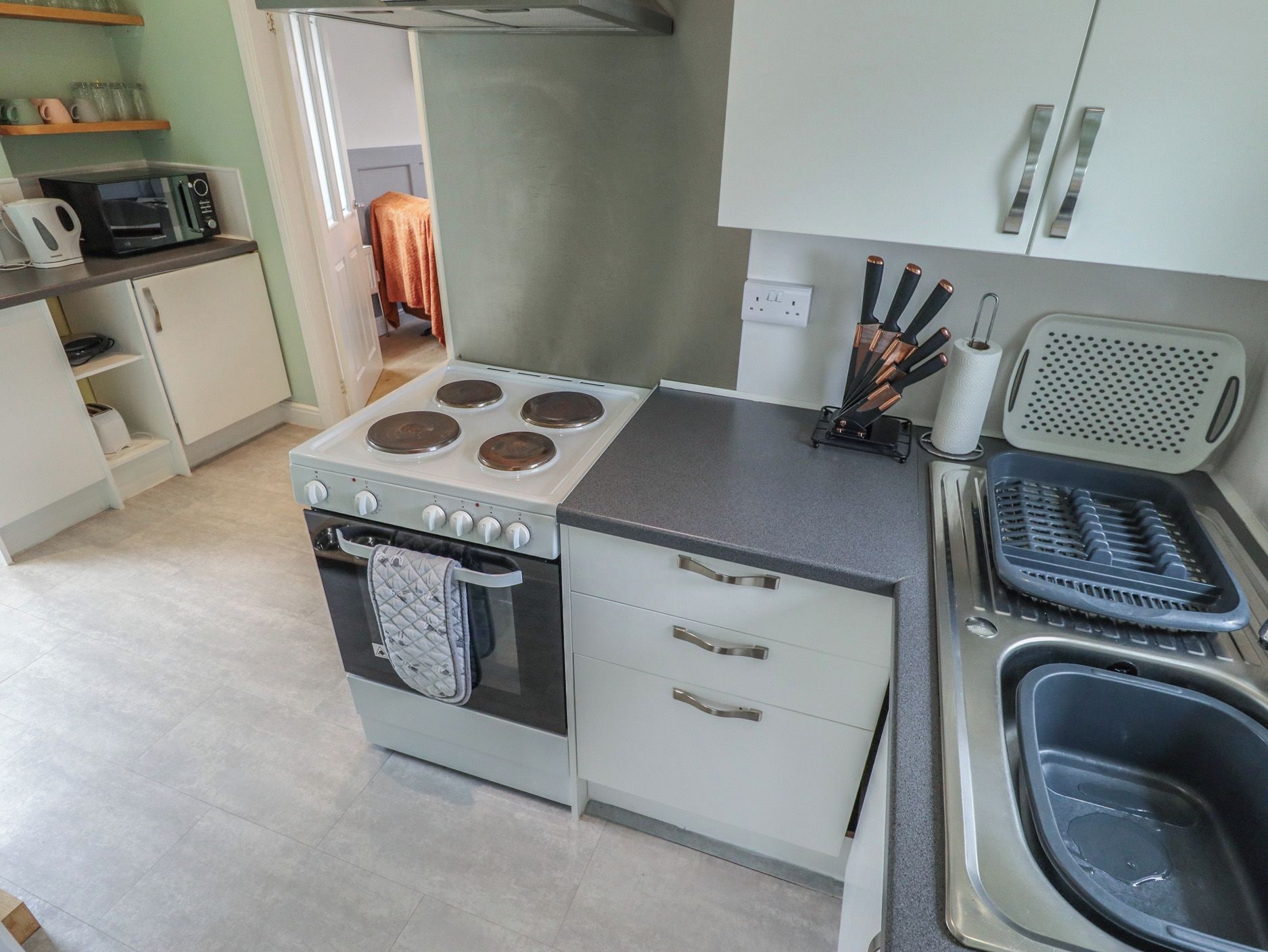 Una cocina con estufa, horno, pileta y una encimera con un bloque de cuchillos y dispensador de toallas de papel.