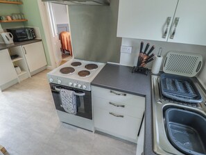 Une cuisine équipée d’une cuisinière, d’un four, d’un évier et d’un plan de travail avec un porte-couteaux et un support pour essuie-tout.