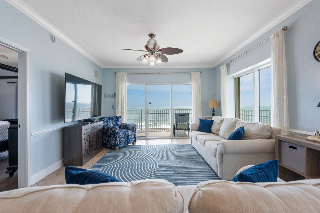 A spacious living room with a large window, a ceiling fan, and a balcony with a view.