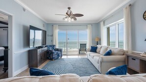 A spacious living room with a large window, a ceiling fan, and a balcony with a view. - Crystal Shores West 208 (Gulf Shores)