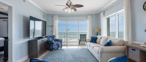 A spacious living room with a large window, a ceiling fan, and a balcony with a view.