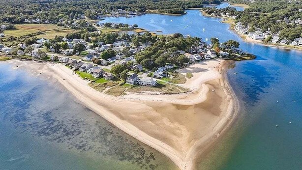 Vue aérienne d’un quartier résidentiel situé sur la côte, avec des maisons le long du littoral et une plage.