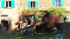 A stone building with blue shutters, a small garden with various plants, and a bench. - Mas la Mayanne in the heart of the vineyards. (Vénéjan)