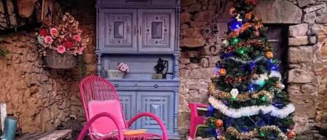Een rustieke kamer met een stenen muur, een blauwe kast, een roze schommelstoel, een kerstboom en een open haard.