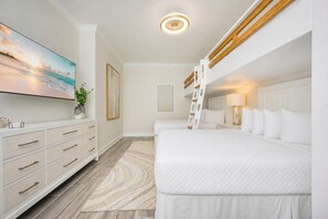 Habitación de hotel con literas, un escritorio con cajones, un cuadro grande y una lámpara en el techo.