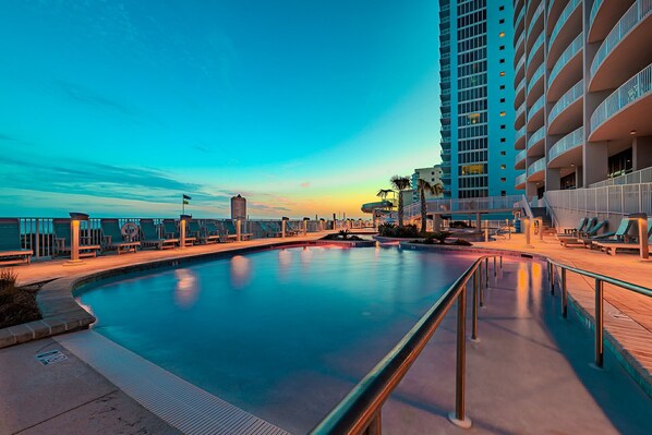 Una piscina con muelle de madera, sillas de descanso y un edificio alto con balcones.