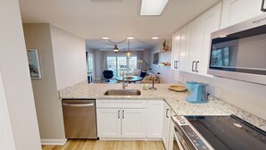 A modern kitchen with white cabinets, a stainless steel dishwasher, a built-in oven, and a large microwave. - Seacrest 714 2 Bedroom Condo (Fort Walton Beach)