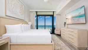 A hotel room with a large bed, a dresser, a desk, and a view of the ocean. - Phoenix Gulf Shores Ii 404 3 Bedroom Condo (Gulf Shores)