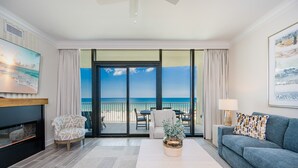 A modern living room with a fireplace, a sofa, a coffee table, and a view of the ocean through large sliding doors. - Phoenix Gulf Shores Ii 404 3 Bedroom Condo (Gulf Shores)