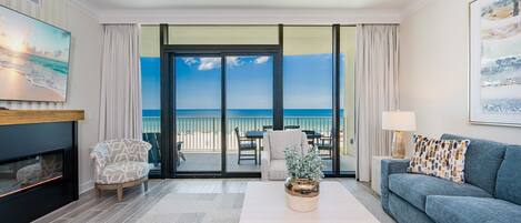 A modern living room with a fireplace, a sofa, a coffee table, and a view of the ocean through large sliding doors.