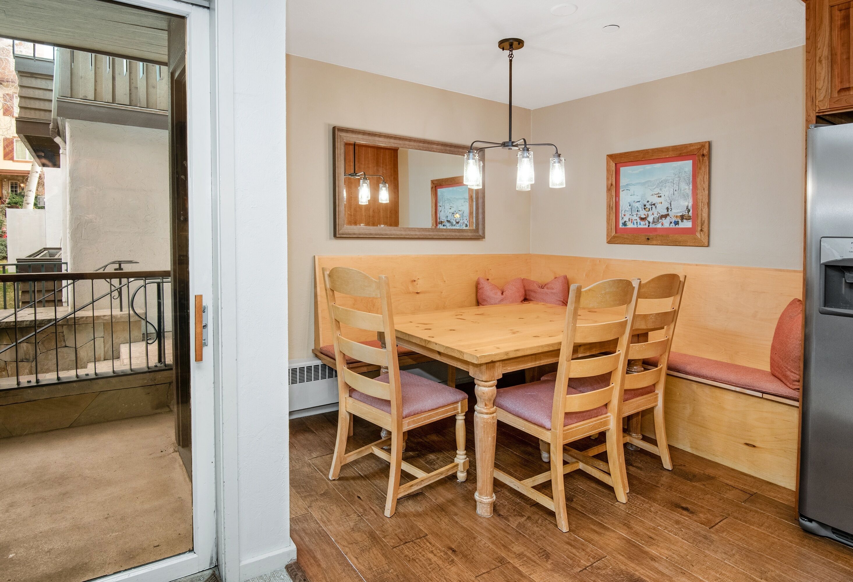 A dining area with a wooden table and chairs, a bench, a mirror, and a refrigerator.