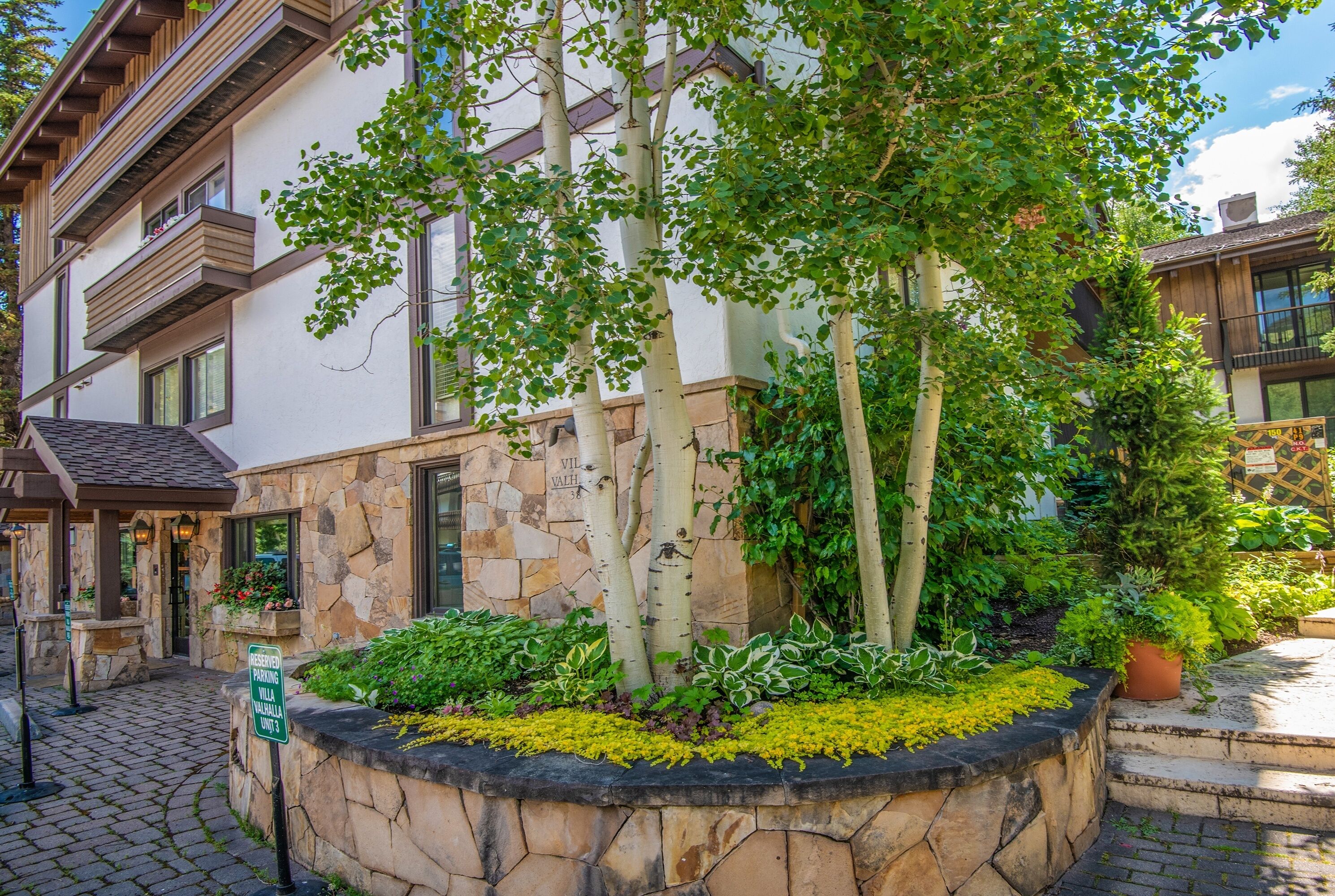 A stone building with balconies, a paved entrance, and a sign indicating reserved parking.