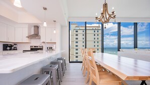 A modern kitchen with a large island, bar stools, and a dining area with a view of the ocean. - Phoenix Gulf Shores Ii 705 4 Bedroom Condo (Gulf Shores)