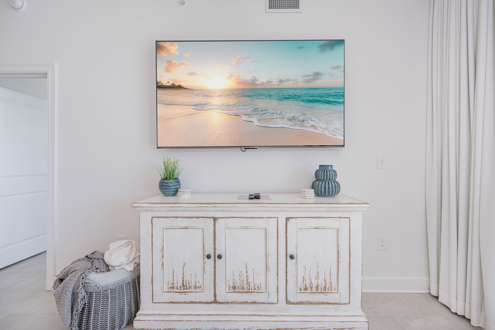 A white cabinet with a television mounted above it, displaying a beach scene.