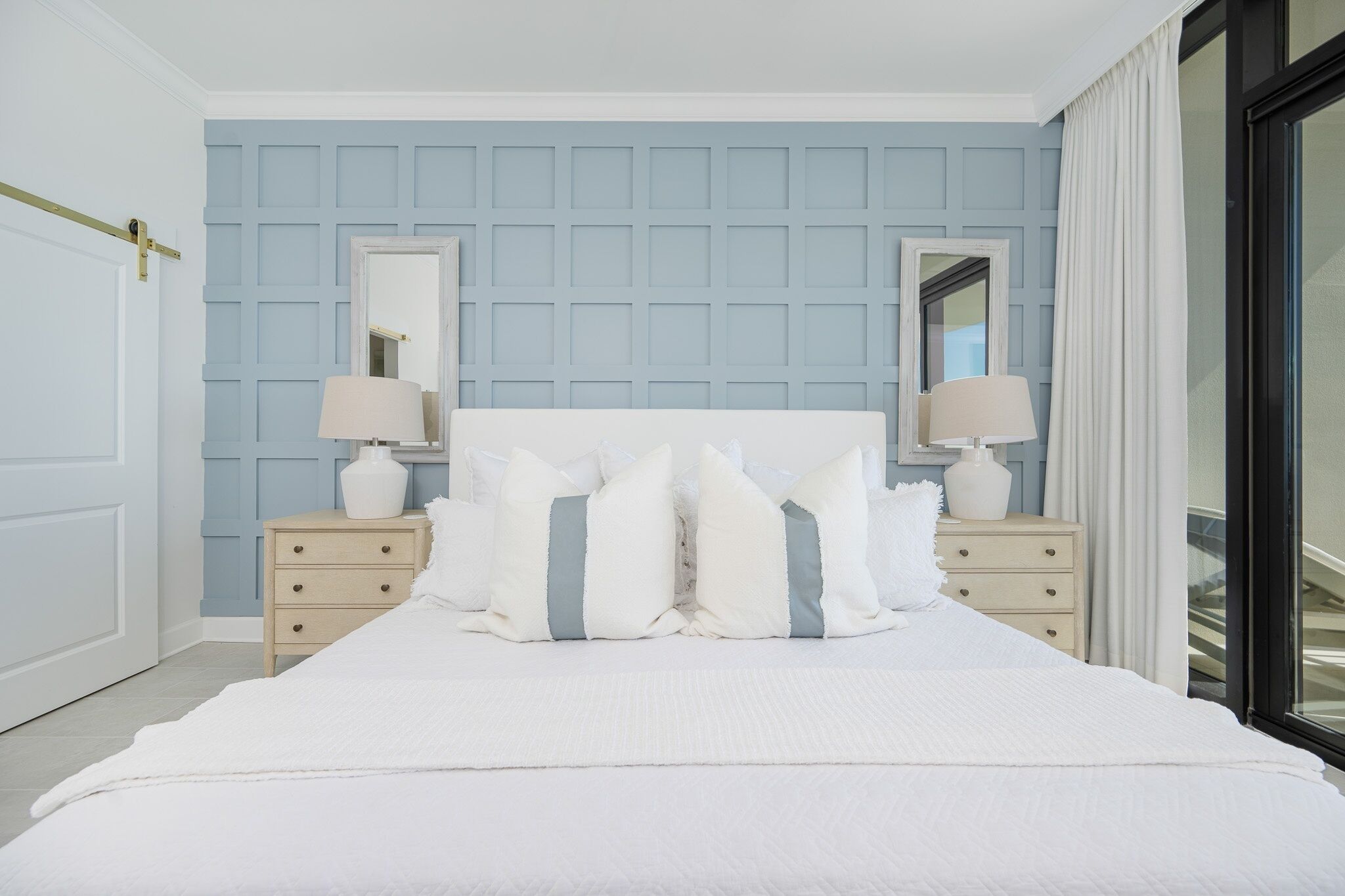 A neatly arranged bedroom with a large bed, two bedside tables with lamps, and a light blue paneled wall.