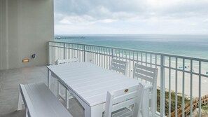 A balcony with a white table and chairs, overlooking a beach and the ocean. - Phoenix Gulf Shores Ii 801 4 Bedroom Condo (Gulf Shores)