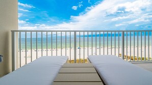 Un balcone con due letti bianchi, vista sulla spiaggia e un cielo azzurro terso.