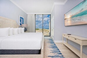 Habitación de hotel con una cama grande, un cuadro, un escritorio y vista a la playa.