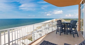 Enjoy stunning beach views from this balcony with a table and chairs.