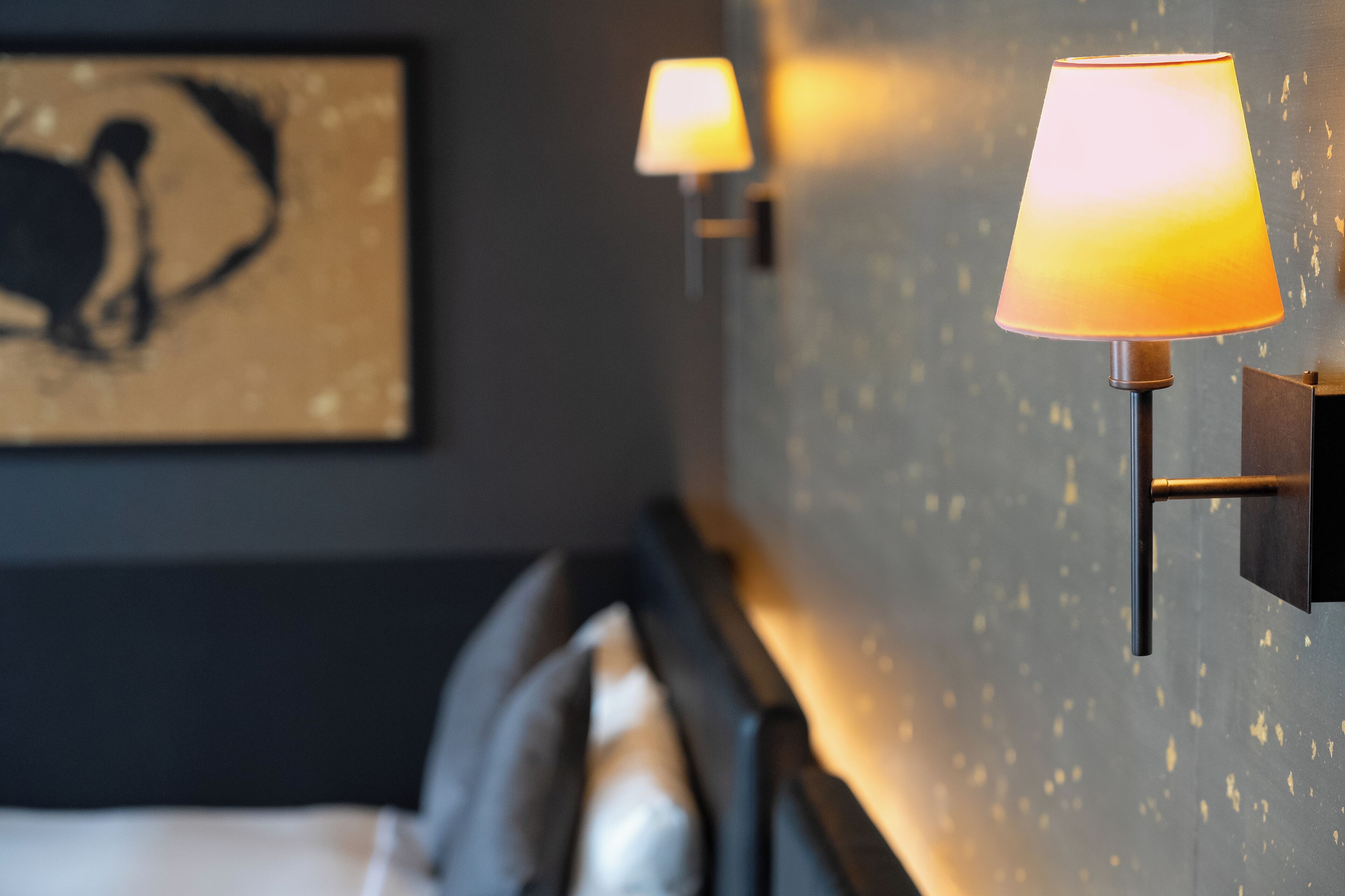 Ett hotellrum med en säng, en sänggavel och två väggmonterade lampor.