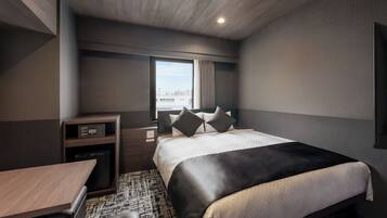 Ein modernes Hotelzimmer mit einem großen Bett, einem Schreibtisch, einem kleinen Kühlschrank und einem Fenster mit Blick auf die Stadt.