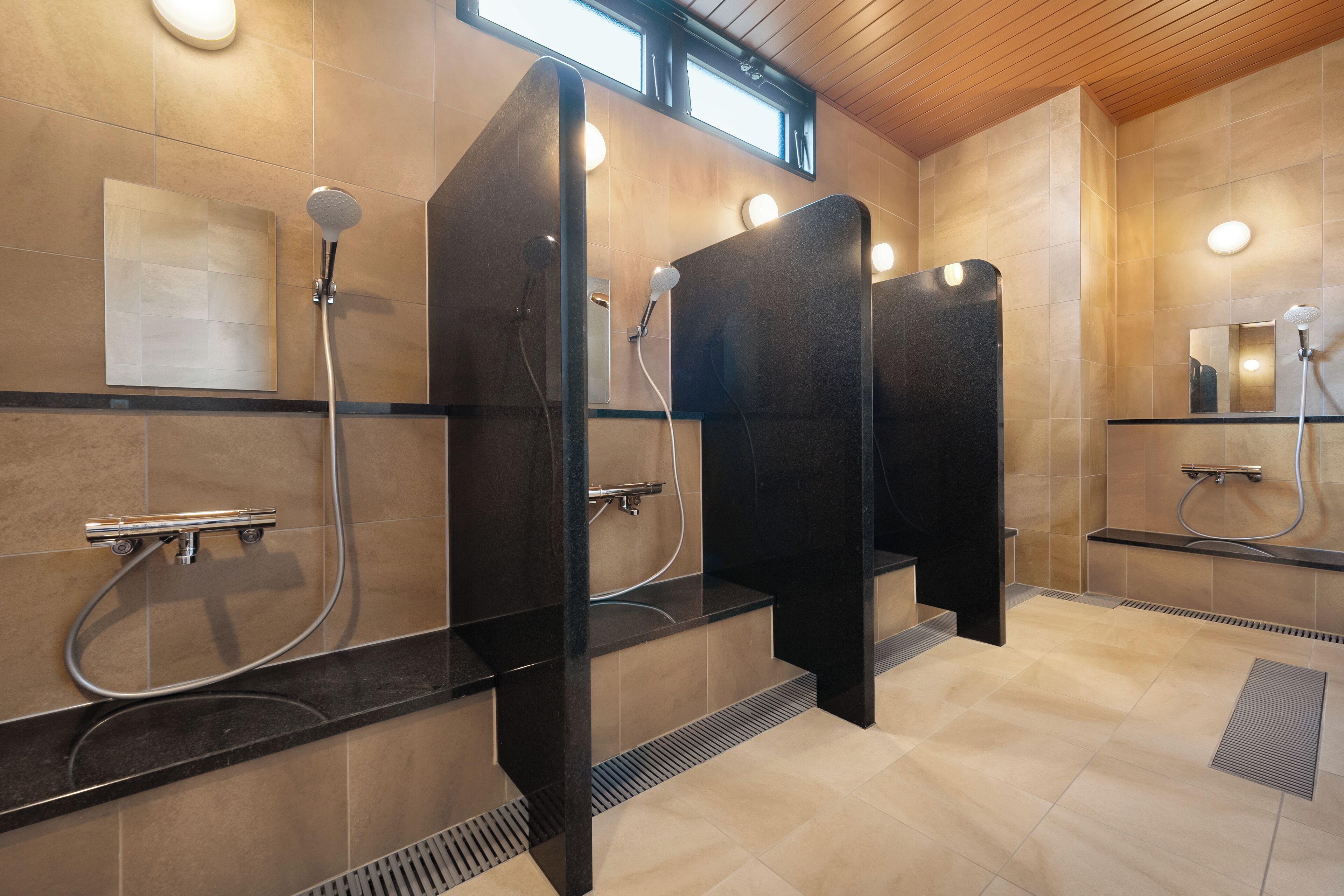 Un baño moderno con cabinas de ducha separadas, tocador con espejo y ventana sobre los lavamanos.