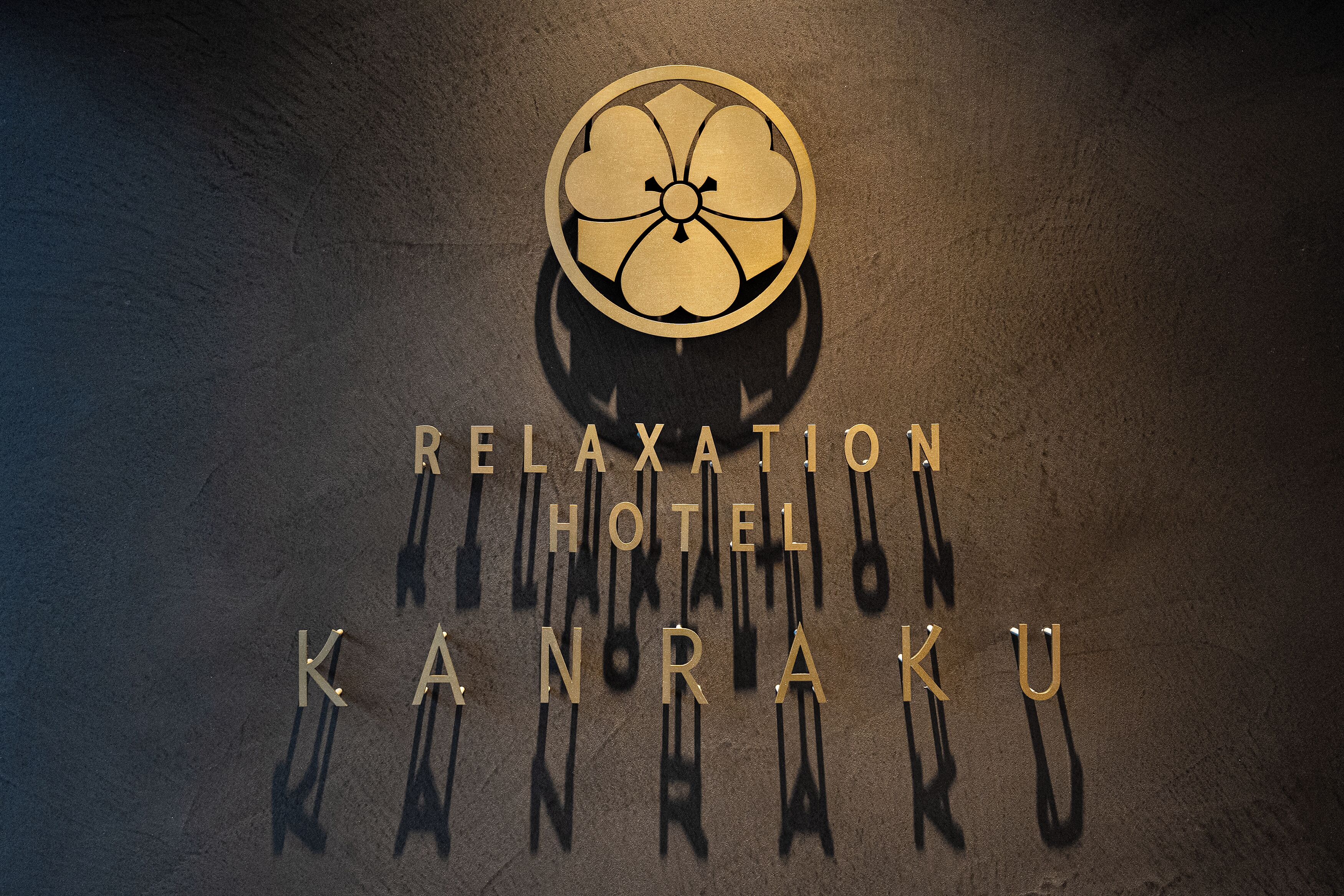 Un logotipo con un emblema circular y el texto 'RELAXATION HOTEL KANRAKU'.