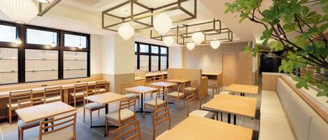 Een modern restaurantinterieur met houten tafels en stoelen, hanglampen en grote ramen.