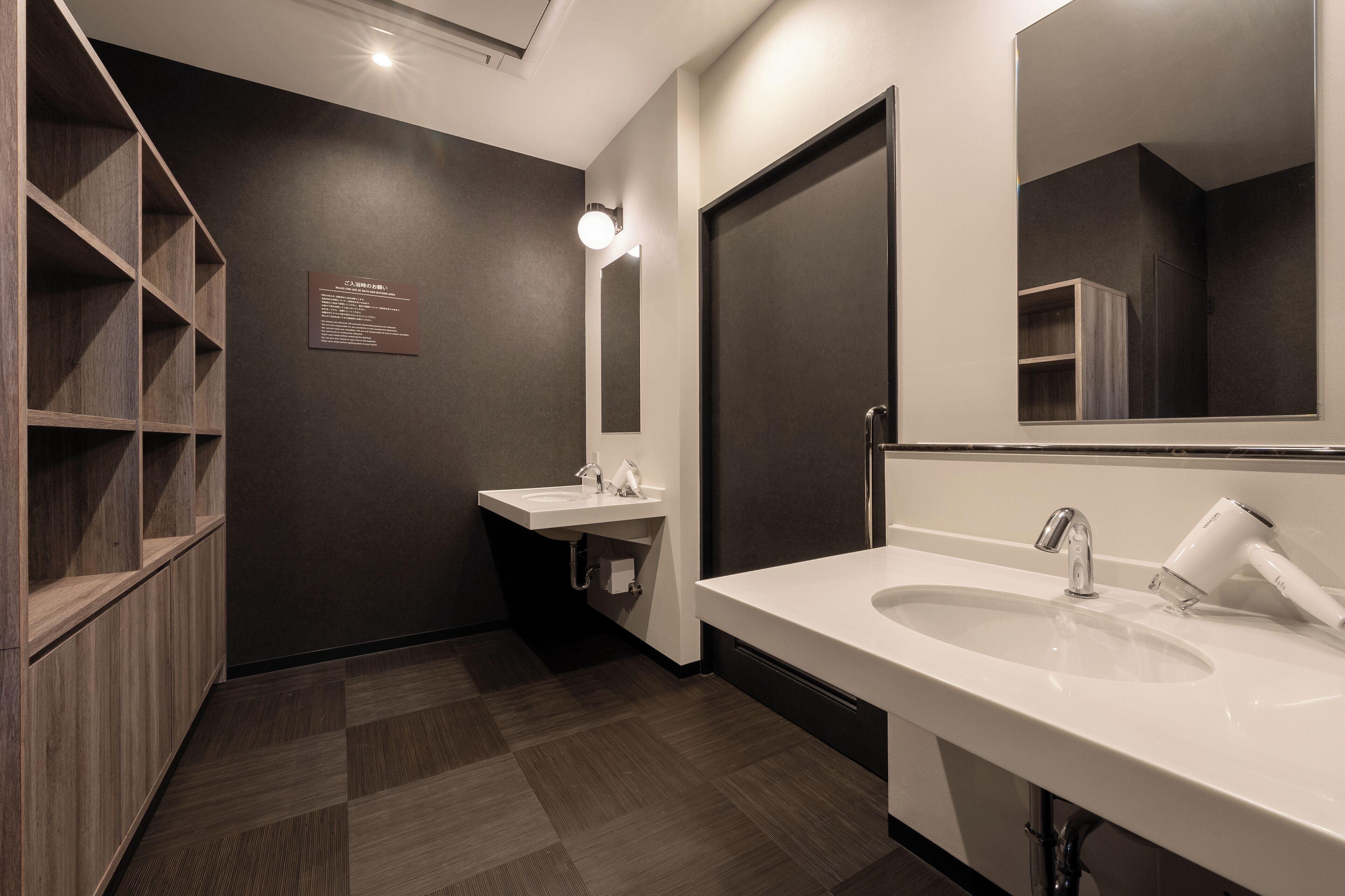 A modern bathroom with a large mirror, two sinks, and a built-in shelf unit.