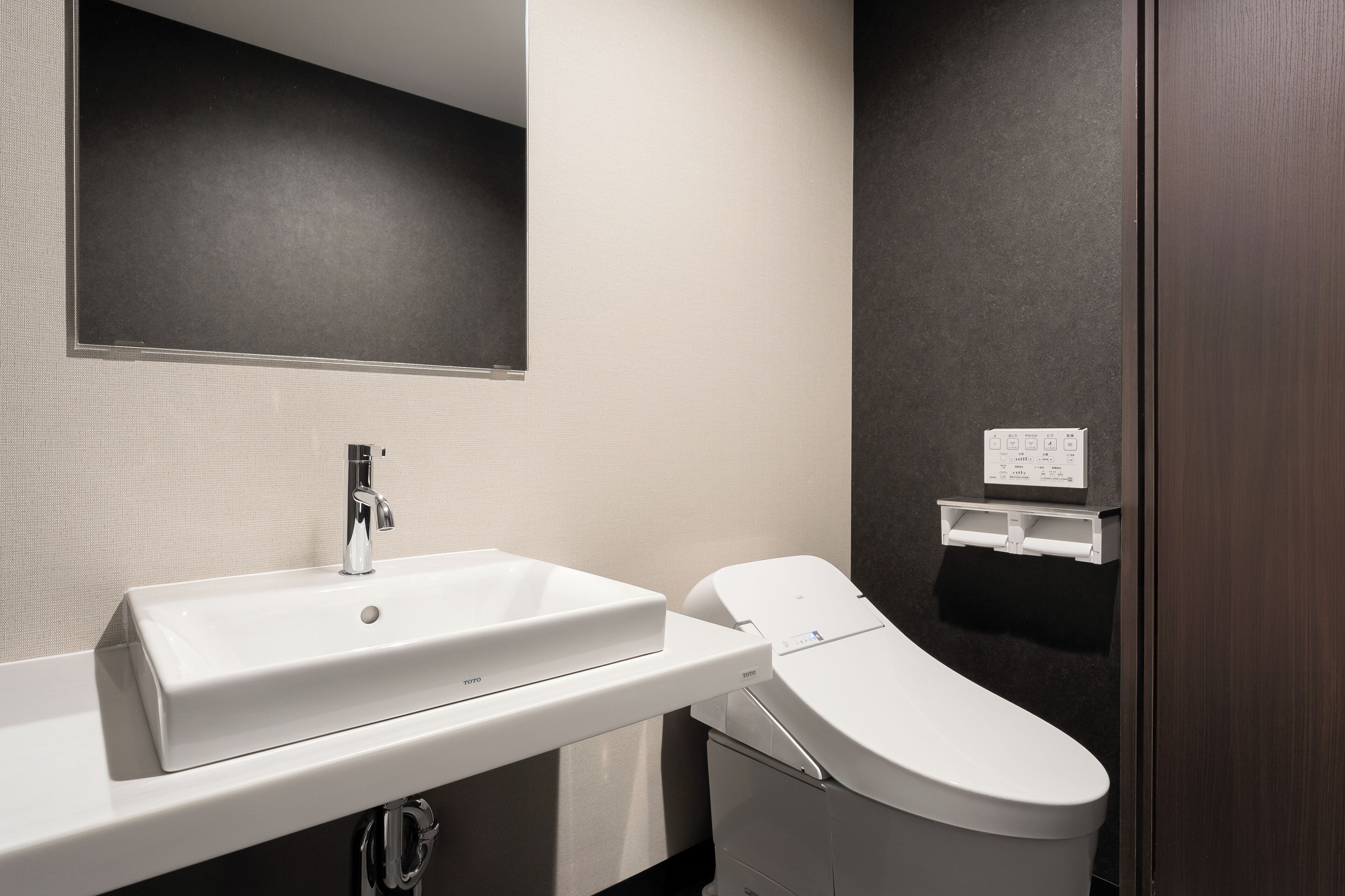 Ein modernes Badezimmer mit einem weißen Waschbecken, einer Toilette und einem Spiegel über dem Waschbecken.