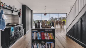 Una cucina moderna con un piano cottura nero, una libreria piena di libri e vista sull'esterno grazie a ampie finestre.