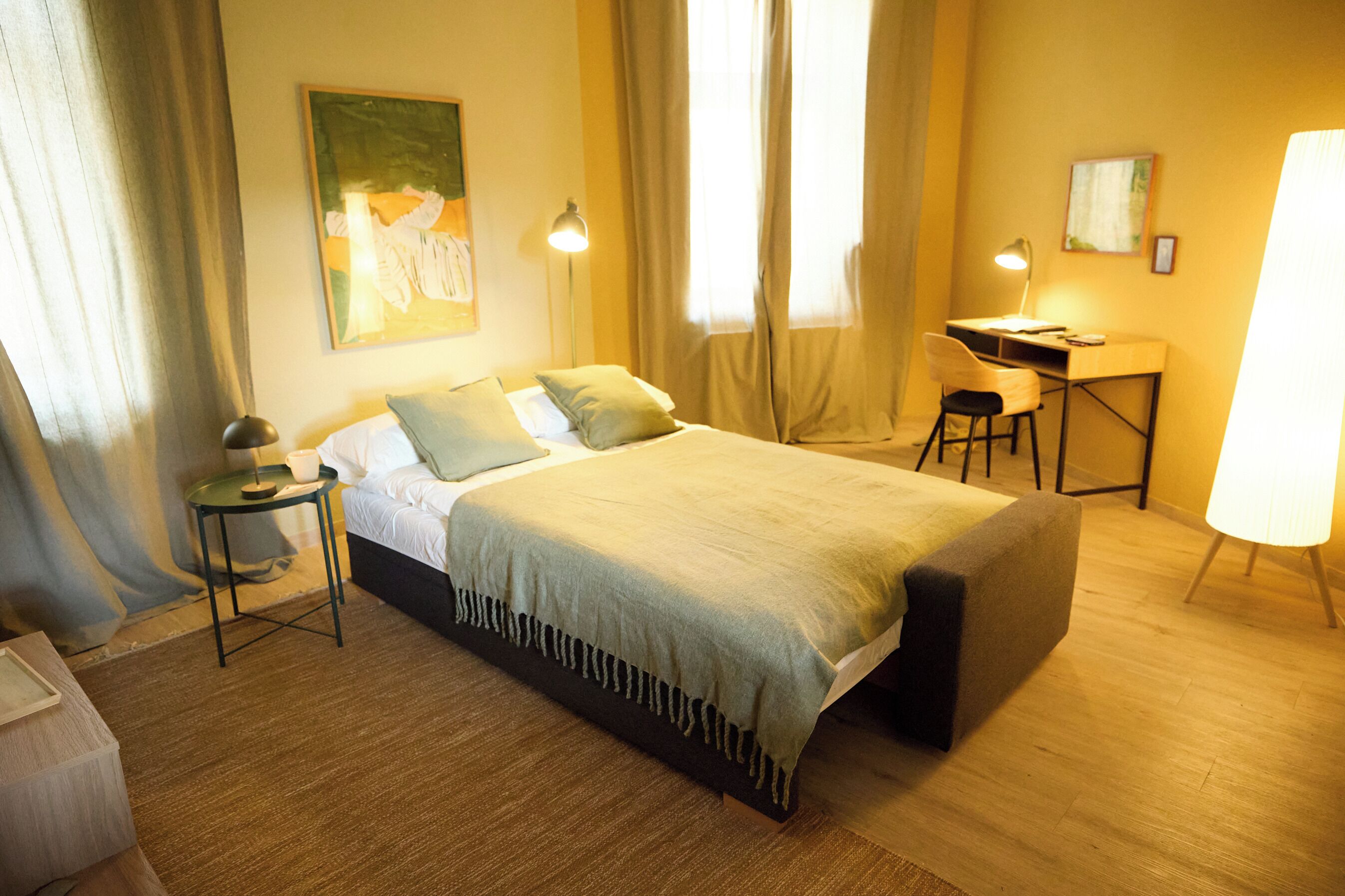 Ein ordentlich eingerichtetes Schlafzimmer mit einem Bett, einem Nachttisch, einer Lampe und einem Schreibtisch mit Stuhl.