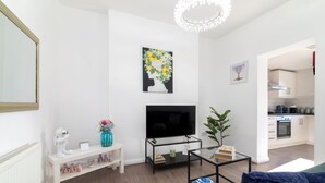 Ein modernes Wohnzimmer mit einem Flachbildfernseher, einem Glastisch, einer Couch und einem kleinen Beistelltisch mit Dekorationselementen.
