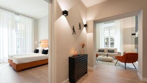 A modern hotel room with a bed, a dresser, and a seating area with a sofa and armchair.
