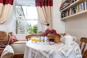 A cozy breakfast setup with a table, bookshelves, and a view of greenery outside. - Cottage in Settle Near Yorkshire Dales (Settle)