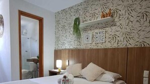 Une chambre d’hôtel avec un grand lit, une tête de lit en bois, un mur orné d’un motif et une petite étagère sur laquelle sont disposés des objets décoratifs.