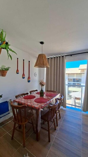A dining area with a table set for six, wooden chairs, a hanging plant, and a view of the outside. - Apartment in cozy Imbassai, 5 minutes from where the river meets the sea - (Mata de São João)