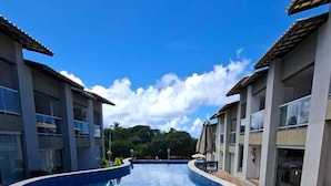 Une piscine à bordures courbes, entourée d’immeubles dotés de balcons, sous un ciel bleu azur.