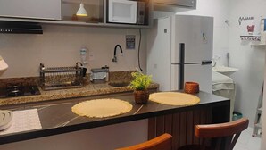 Une cuisine moderne équipée d’un four à micro-ondes, d’une cuisinière et d’un réfrigérateur. On y trouve deux lampes suspendues, un évier et une petite plante en pot sur le plan de travail.