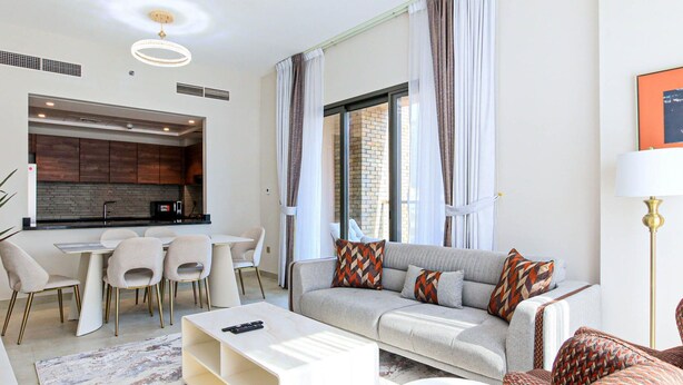 A modern living room with a grey sofa, a coffee table, and a dining area with a kitchen in the background.