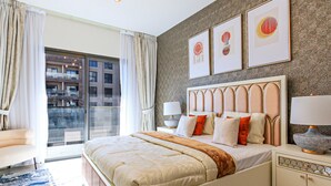 A hotel room with a large bed, a nightstand, a lamp, and a view of a building through a glass door.