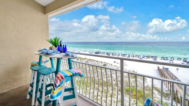 A balcony with a view of the beach, a table with chairs, and a potted plant. - 🐬Crystal Sands 306B - Summer Salt | Gulf Views + Heated Community Pool (Destin)